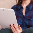 woman in blue denim button up jacket holding white laptop computer