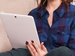 woman in blue denim button up jacket holding white laptop computer