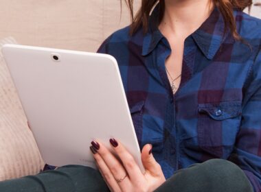 woman in blue denim button up jacket holding white laptop computer