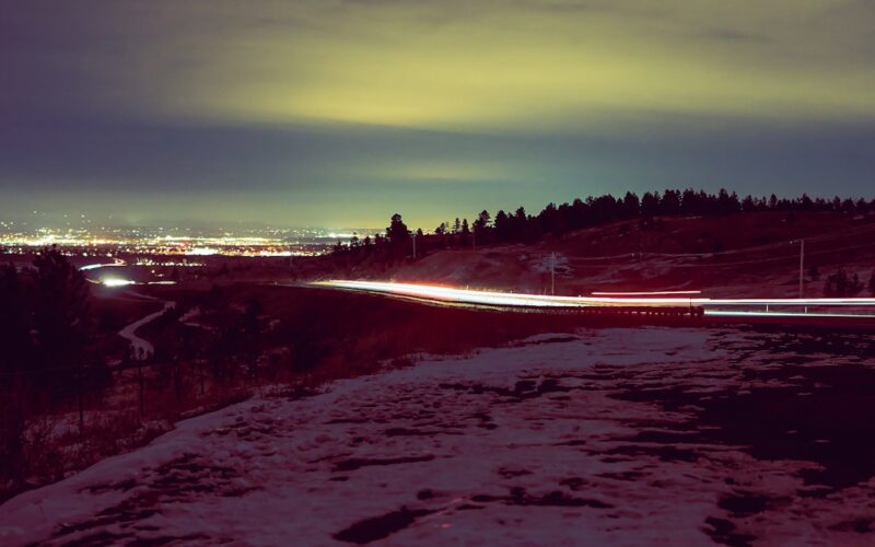 a snowy landscape with a road and trees in the background