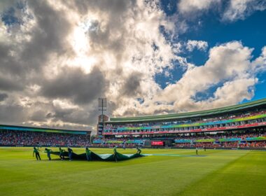 Cricket stadium with groundsmen covering the pitch.