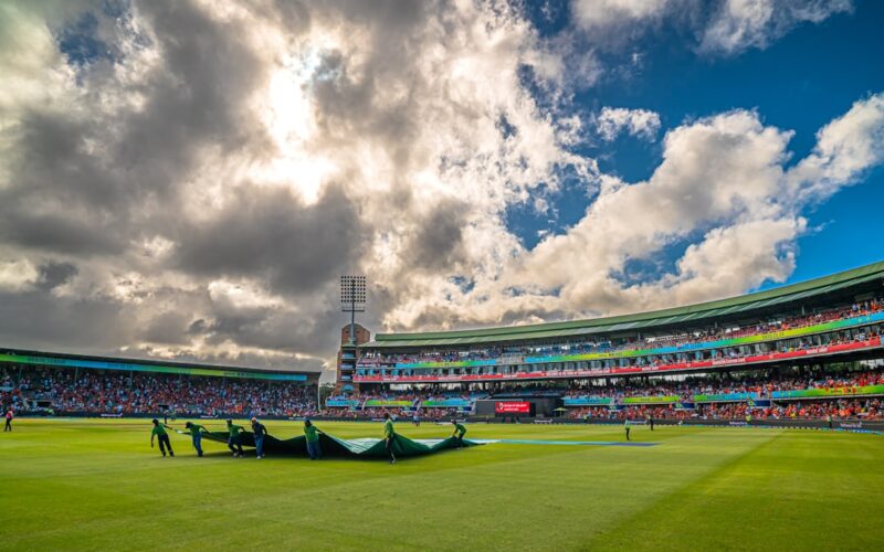 Cricket stadium with groundsmen covering the pitch.