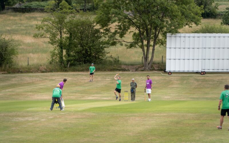 People are playing cricket on a grassy field.