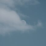 a plane flying in the sky with a half moon in the background