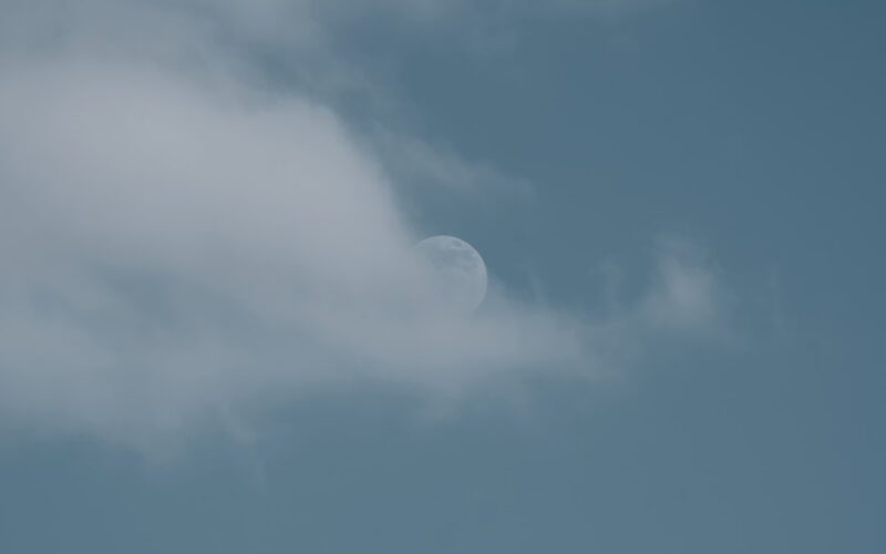 a plane flying in the sky with a half moon in the background