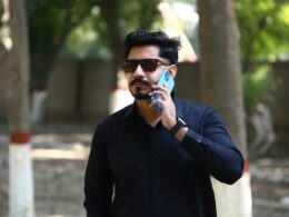 Man in black shirt talking on a blue phone.