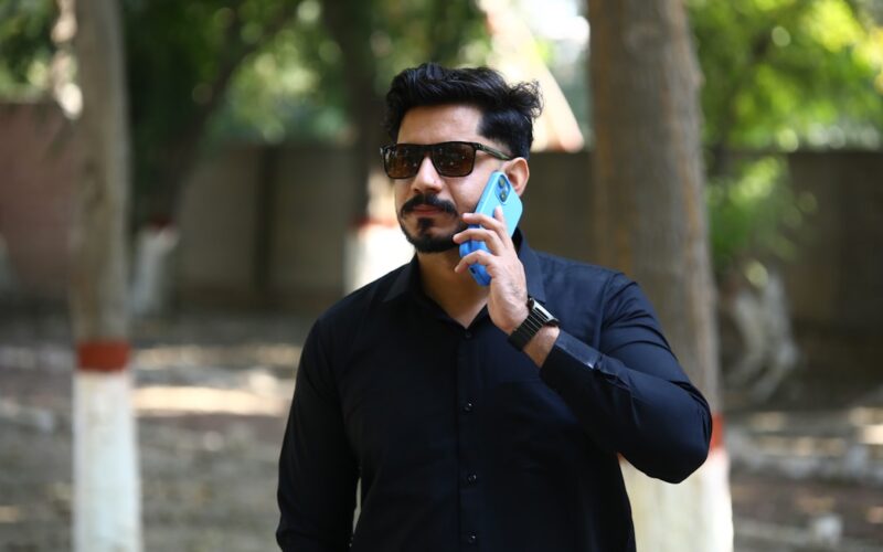 Man in black shirt talking on a blue phone.