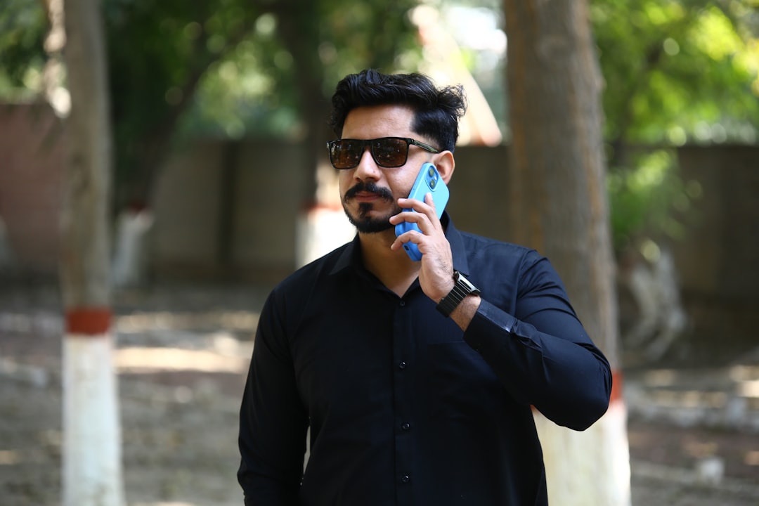 Man in black shirt talking on a blue phone.