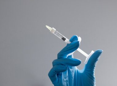 A hand in a glove holds a syringe.