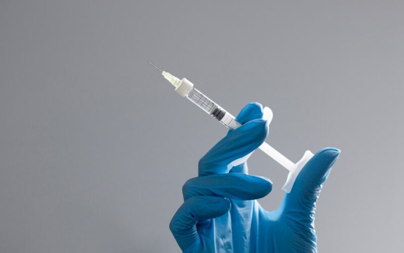 A hand in a glove holds a syringe.