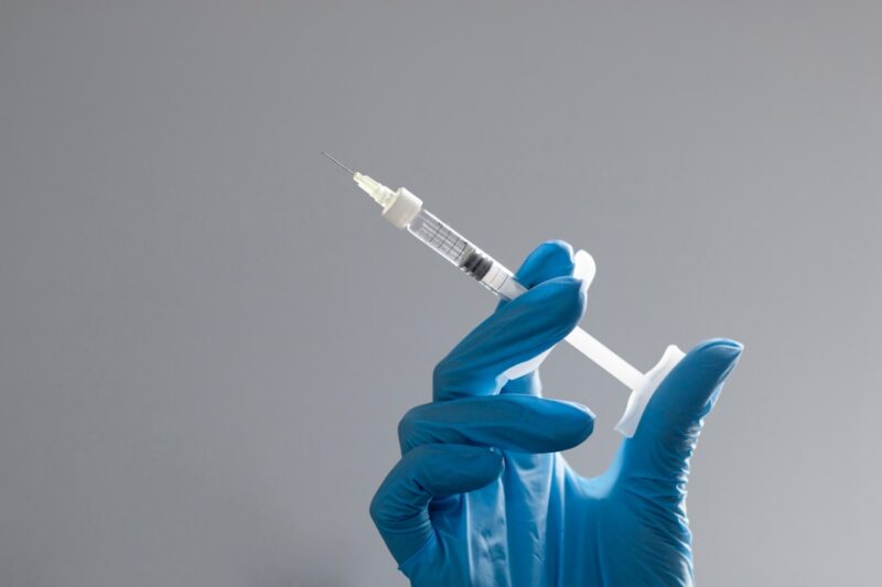 A hand in a glove holds a syringe.