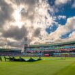 Cricket stadium with groundsmen covering the pitch.