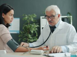 Doctor checks patient's blood pressure with stethoscope.