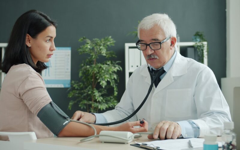 Doctor checks patient's blood pressure with stethoscope.