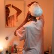 Woman applying towel to hair in bathroom mirror.