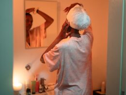 Woman applying towel to hair in bathroom mirror.