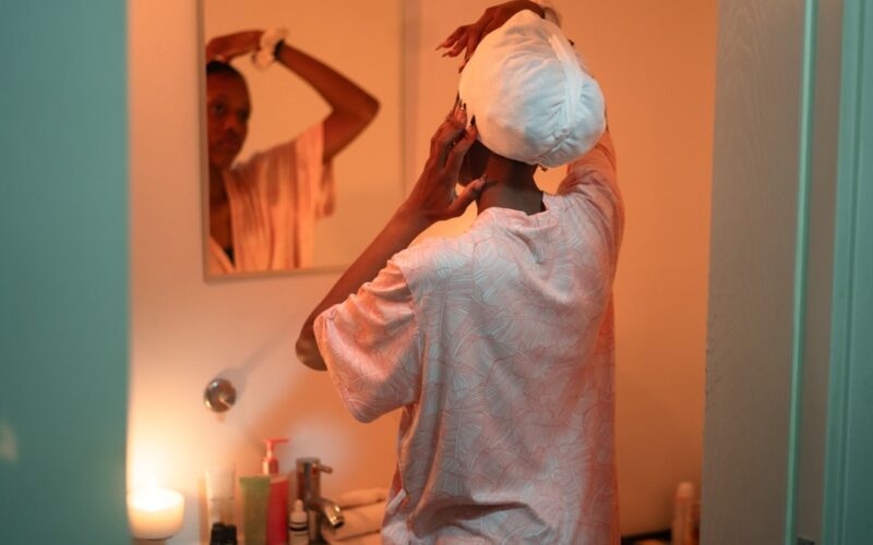 Woman applying towel to hair in bathroom mirror.