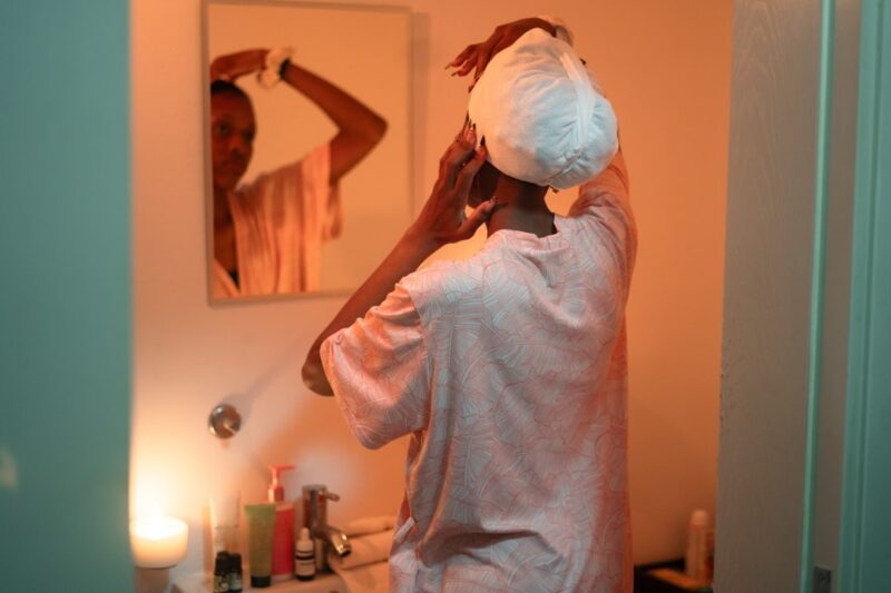 Woman applying towel to hair in bathroom mirror.