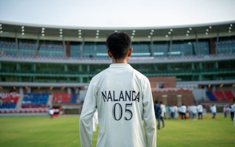 Young cricketer stands on field before stadium crowd.