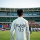 Young cricketer stands on field before stadium crowd.