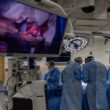 Surgeons operate while viewing the procedure on a large screen.