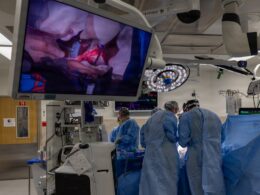 Surgeons operate while viewing the procedure on a large screen.