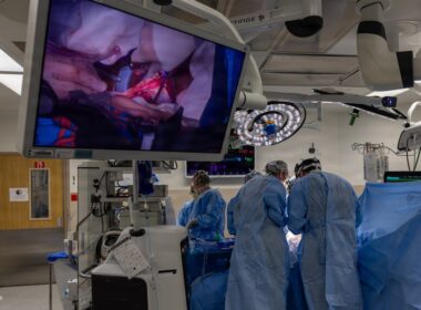 Surgeons operate while viewing the procedure on a large screen.