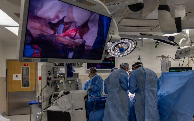 Surgeons operate while viewing the procedure on a large screen.