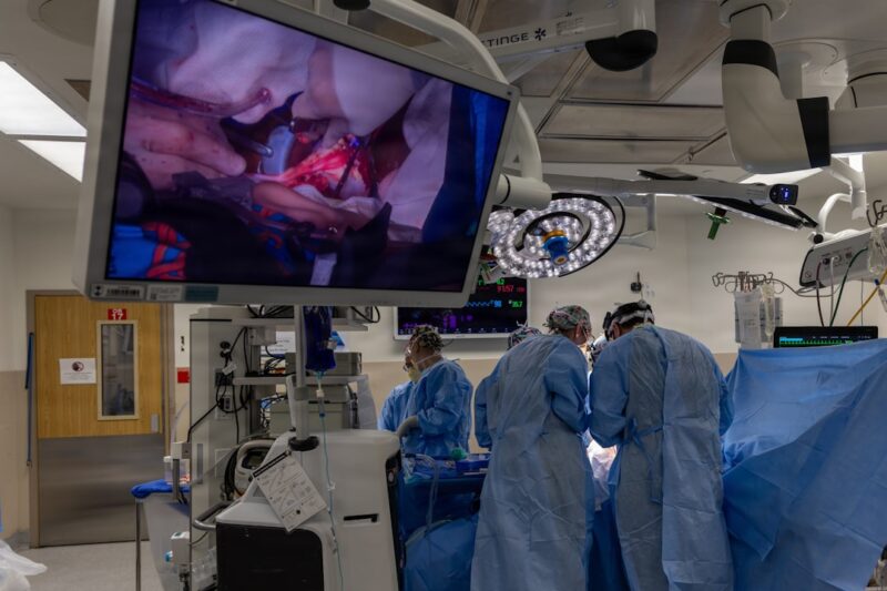 Surgeons operate while viewing the procedure on a large screen.