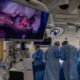 Surgeons operate while viewing the procedure on a large screen.