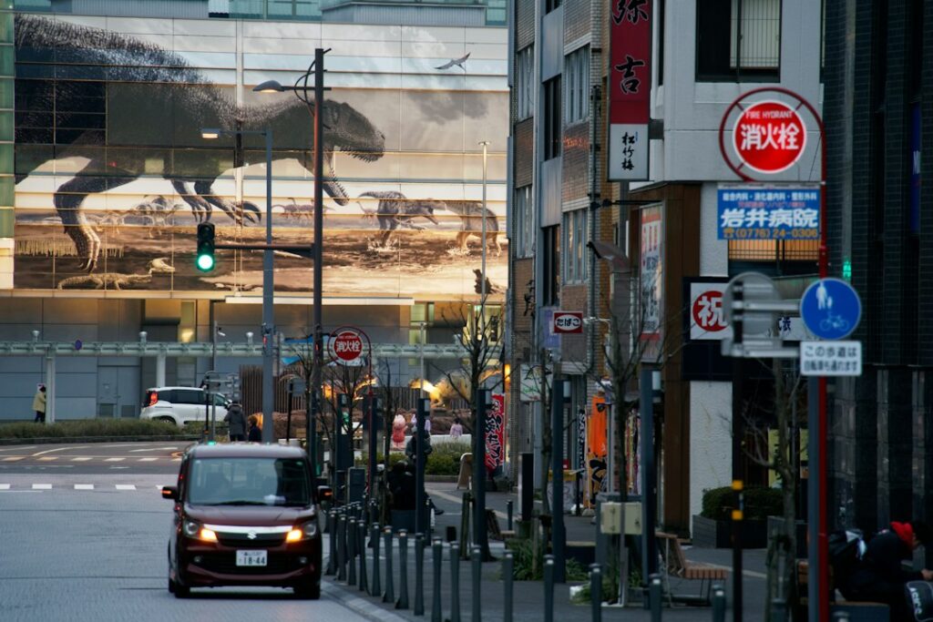 A car driving on a city street past a building with a large dinosaur mural