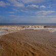 Muddy ocean waves crash onto a sandy beach