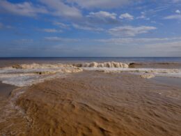 Muddy ocean waves crash onto a sandy beach