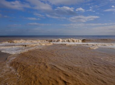Muddy ocean waves crash onto a sandy beach