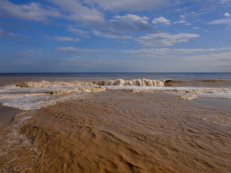 Muddy ocean waves crash onto a sandy beach