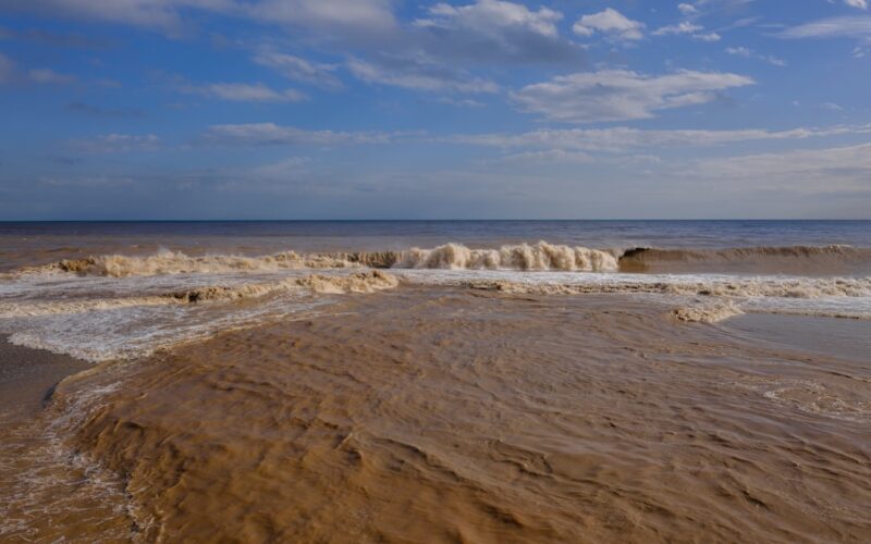 Muddy ocean waves crash onto a sandy beach