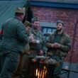 Men in vintage military uniforms gathered around a fire