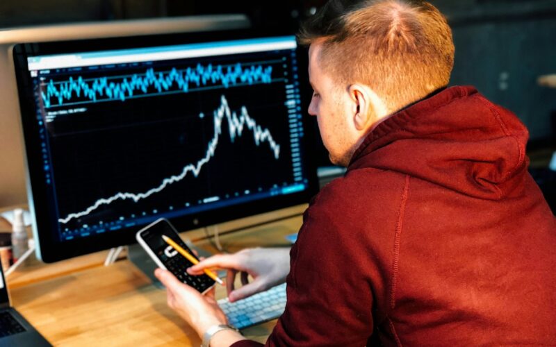 man holding black smartphone with flat screen monitor in front
